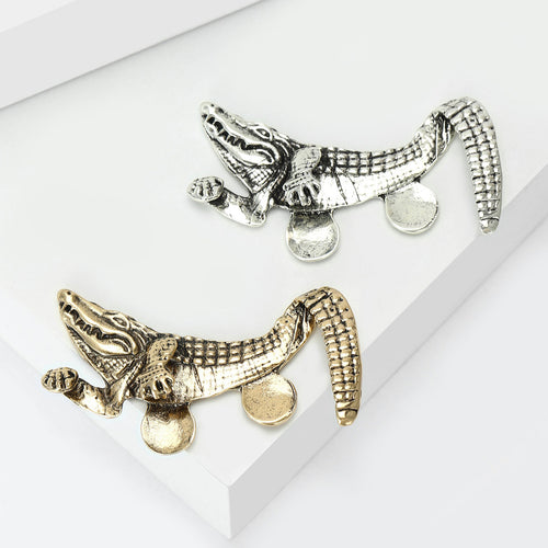 Gold and silver crocodile brooches side by side on white blocks