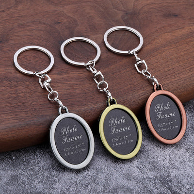 Three oval photo frame keychains in bronze, silver, and copper tones rest on a wooden surface.