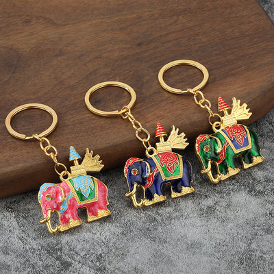 Three pink, blue, and green elephant keychains displayed on wood and gray fabric.