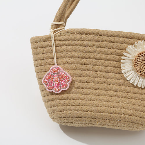 Pink beaded seashell charm tied to the handle of a woven straw tote bag