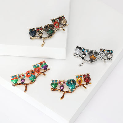 Five small jeweled owls perched together on a branch shown on a white background.