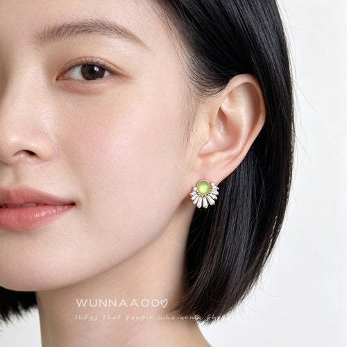 Gold-tone clear-stone-sunburst green-round studs shown worn on an ear.