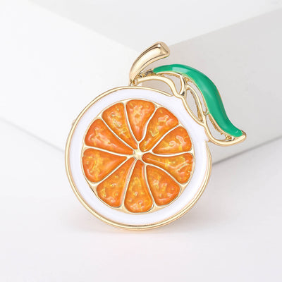 Orange enamel citrus slice brooch with green leaf on white block