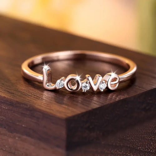 Rose gold LOVE ring resting on dark wood block front view