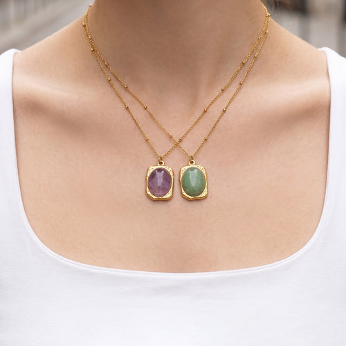Model wearing crossed gold purple and green oval stone pendant necklaces