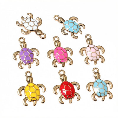 Overview of small turtle charms with antique gold-tone outlines and colorful enamel shells arranged on a light backgroun