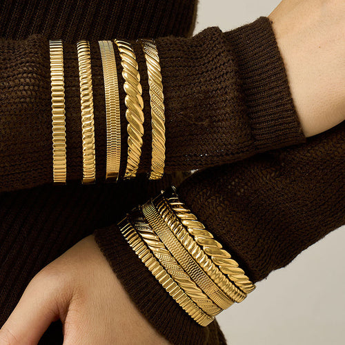 Stacked gold textured hinge bangles on wrist over brown sweater