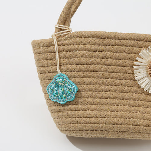 Turquoise beaded seashell charm tied to the handle of a woven straw tote bag