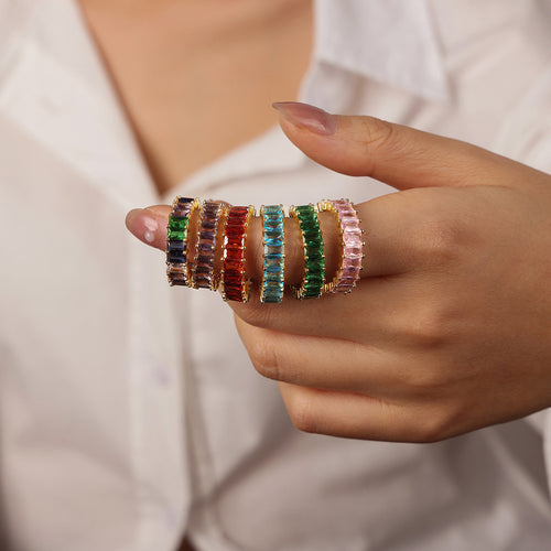 Hand wearing stack of gold baguette zircon rings in mixed colors
