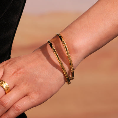 Two gold bamboo segment bangles stacked on wrist outdoors