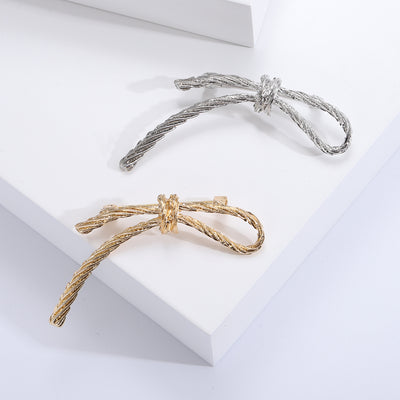 Silver and gold twisted rope bow brooches on white steps