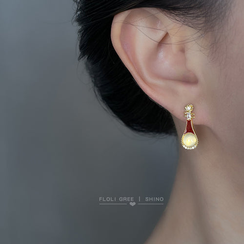 Gold-tone burgundy lute-shaped white-cabochon studs shown worn on an ear.