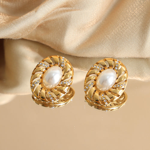 Pair of gold oval swirl pearl crystal studs on reflective surface with fabric