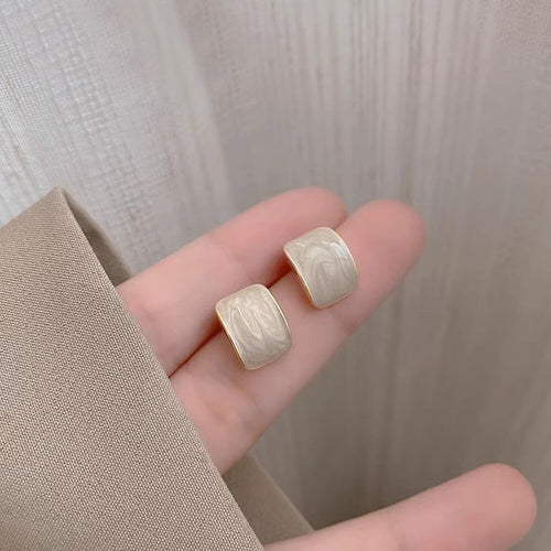 Pair of cream enamel square studs resting on fingers close-up