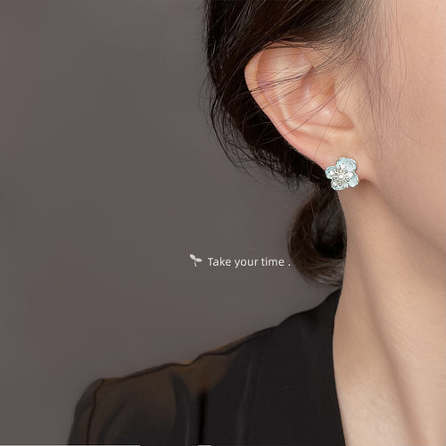 Pale aqua translucent flower and pearl stud earrings shown worn on an ear.