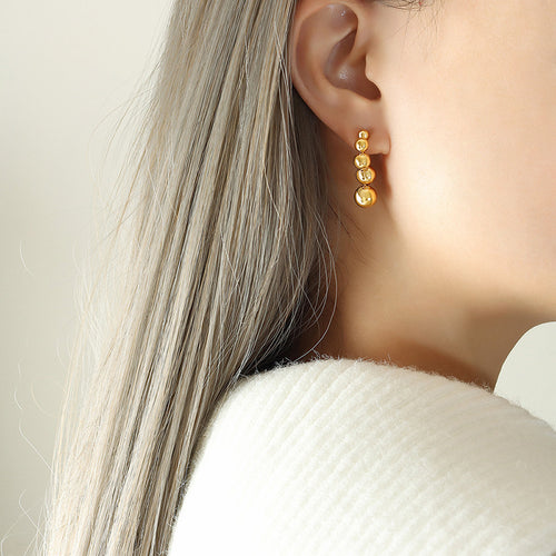 Gold graduated ball drop stud earring worn on ear side profile