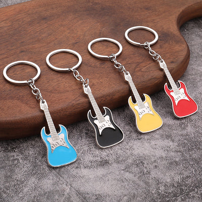 Four silver-tone guitar keychains in light blue, black, yellow, and red on a wooden board.