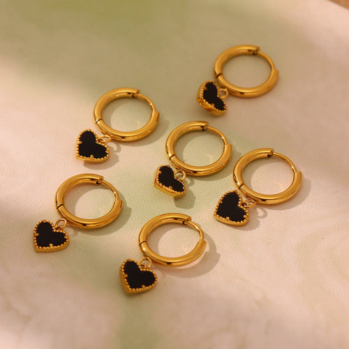 Several gold black heart dangle hoops on soft fabric