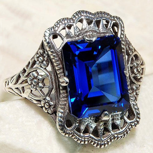 Styled view of royal blue rectangular crystal filigree ring in silver tone