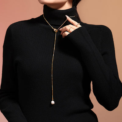 Gold lariat necklace with pearl drop worn on black turtleneck