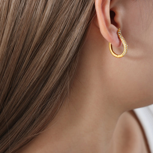 Gold U-shape clear crystal huggie earring worn on model with brown hair