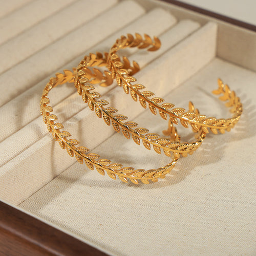 Two gold leaf branch open cuffs on cream jewelry tray