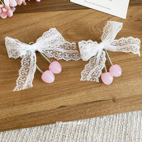 Two white lace bow pink cherry duckbill clips laid on wooden board