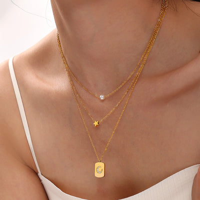 Model wearing layered gold star and pearl necklaces with tag pendant
