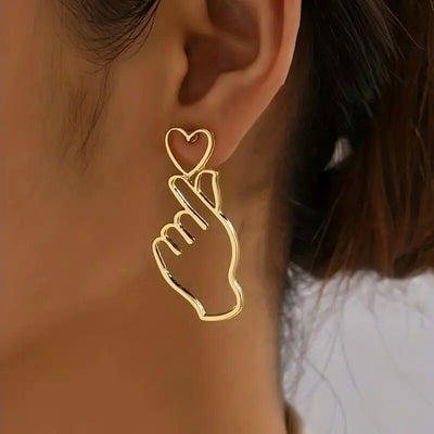 Gold outline finger heart gesture stud earring worn on model ear
