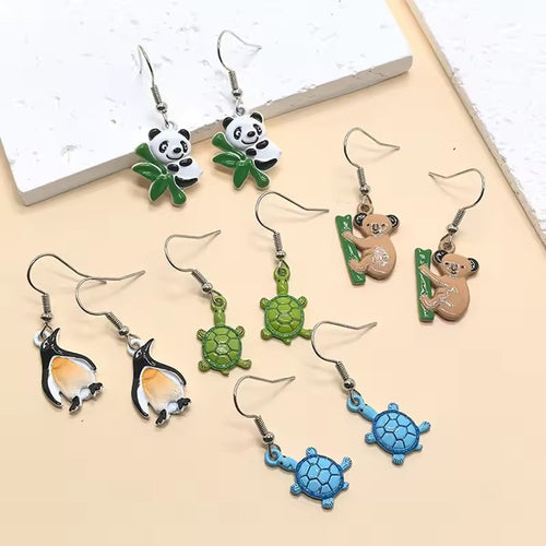 Assorted panda turtle koala and penguin enamel animal earrings on beige surface