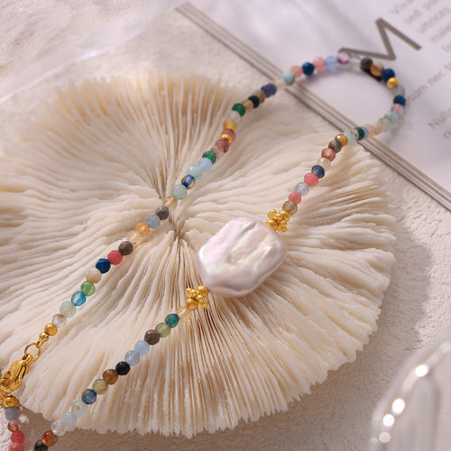Close-up of baroque pearl center on multicolor beads over white shell
