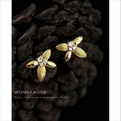 Gold four-petal crystal flower studs beside dark pinecone