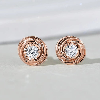 Pair of rose gold swirl clear center stud earrings on white surface