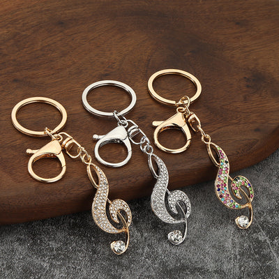 Three treble clef keychains in silver-tone and gold-tone finishes rest on a wooden surface.