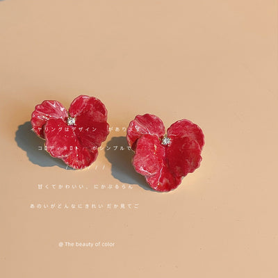 Magenta enamel flower ear clips on beige background