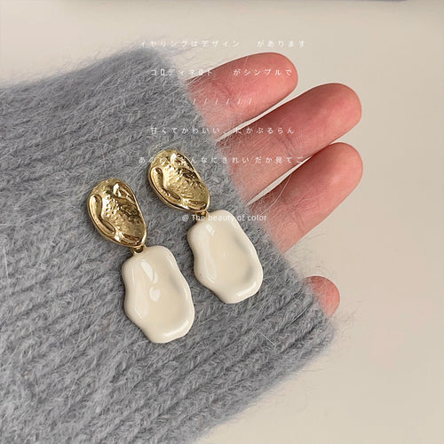 Gold hammered stud white enamel drops held against gray sweater