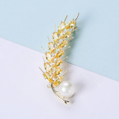 Front view of golden wheat-ear brooch with champagne crystals and pearl accent against a white background.