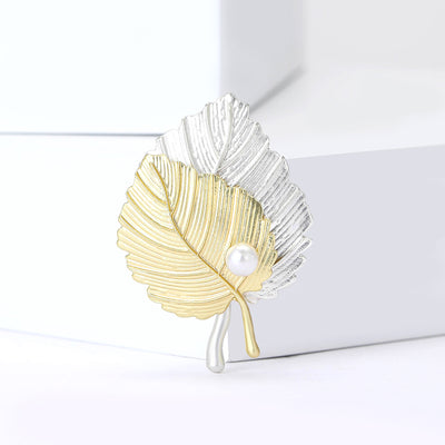 Matte gold and silver dual-leaf brooch with pearl accent on white blocks