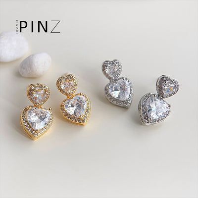 Gold and silver double heart halo zircon drop studs on beige with pebbles