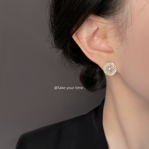 Gold-tone pink-green patterned-round-medallion studs shown worn on an ear.