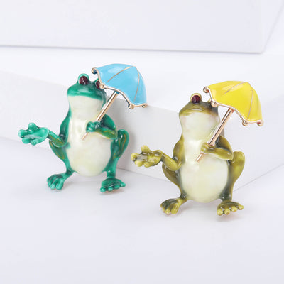 Front view of the umbrella frog brooch showing a green frog holding a bright umbrella with a pearl-look belly