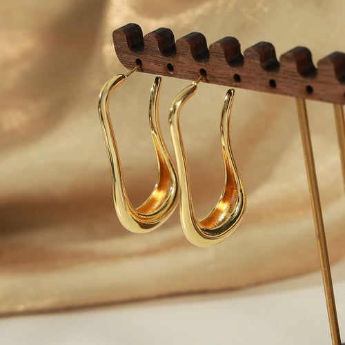 Pair of gold goose neck earrings hanging on wooden stand