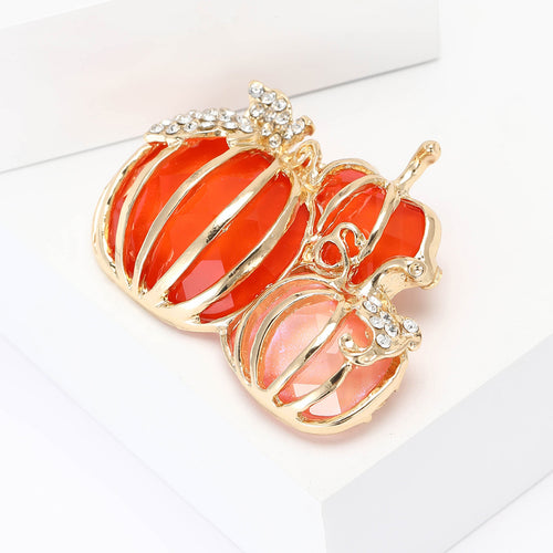 Three orange and pink pumpkins topped by a crystal leaf shown in a styled display.