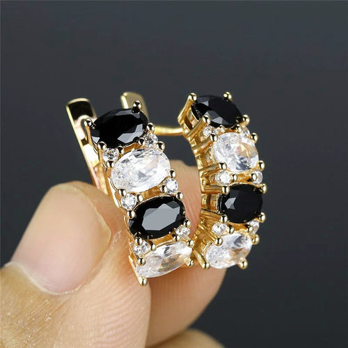Gold black-clear oval CZ huggies held between fingers side view