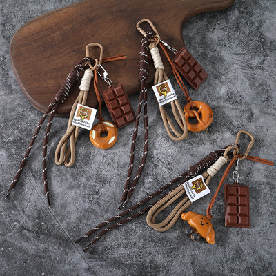 Three cord keychains with different brown bread charms and chocolate bars rest beside a wooden board.