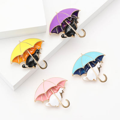 A black cat sheltered beneath a bright enamel umbrella shown on a white background.