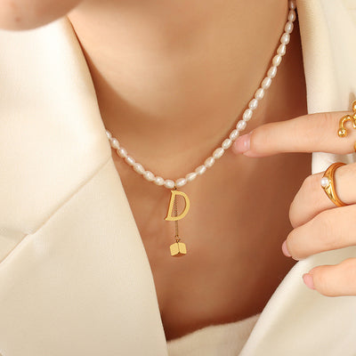 Model wearing white pearl necklace with gold D and cube tassel