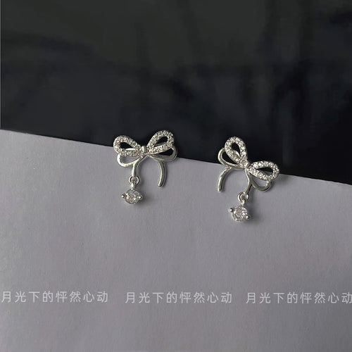 Silver clear pavé bow studs with drops on gray surface