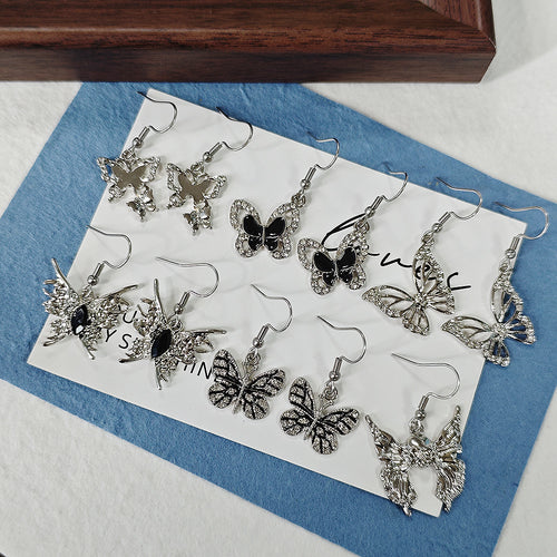 Assorted silver butterfly drop earring pairs on white card over blue cloth