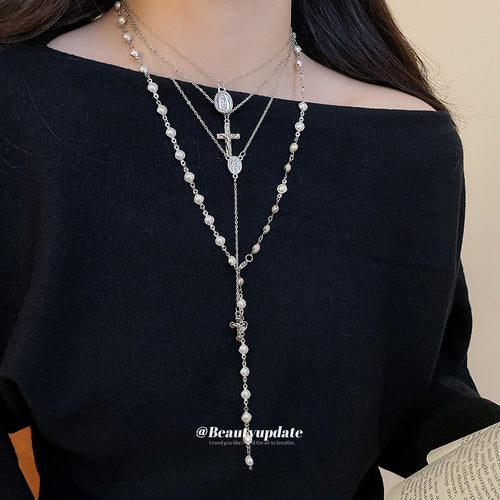 Layered silver cross and pearl necklaces worn on black off-shoulder top